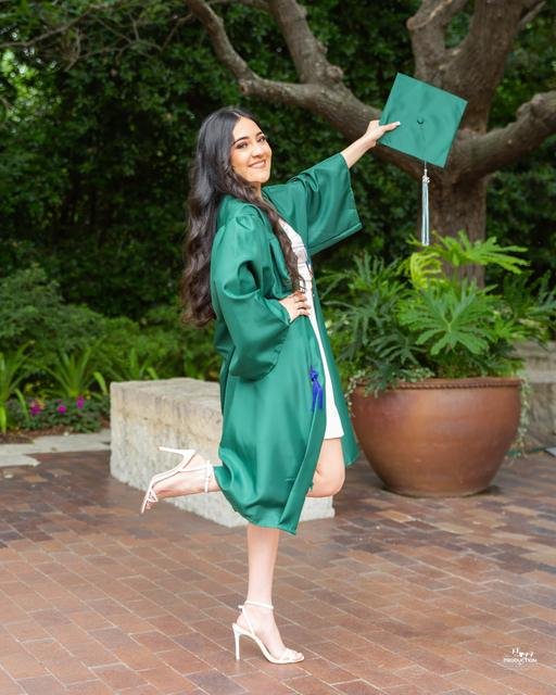 Graduada con toga verde lanzando su birrete en un jardín